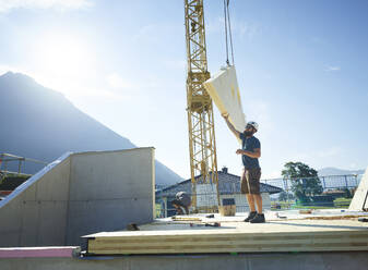 Zimmermann arbeitet auf dem Dach mit Hilfe eines Krans auf der Baustelle - CVF02118