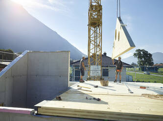 Kollegen arbeiten auf dem Dach mit Hilfe eines Krans auf der Baustelle - CVF02119