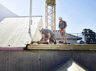 Zimmermann beim Verlegen des Daches auf der Baustelle an einem sonnigen Tag - CVF02134