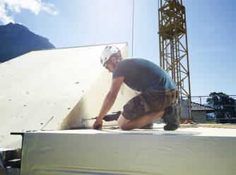 Junger Zimmermann mit Bohrmaschine beim Verlegen des Dachs auf der Baustelle an einem sonnigen Tag - CVF02135