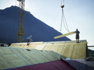Arbeiter bei der Montage des Daches mit Hilfe eines Krans auf der Baustelle - CVF02136