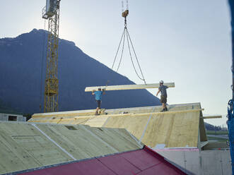 Zimmerleute bei der Dachmontage mit Hilfe eines Krans auf der Baustelle - CVF02137