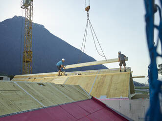 Zimmerleute bei der Montage eines Daches mit einem Kran auf der Baustelle - CVF02138