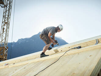 Zimmermann bei der Arbeit mit einer Bohrmaschine auf dem Dach einer Baustelle - CVF02140