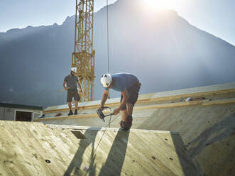 Carpenter working with drill on wooden roof at construction site - CVF02151