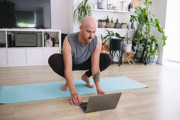 Mann benutzt Laptop auf Trainingsmatte zu Hause - ASGF02592