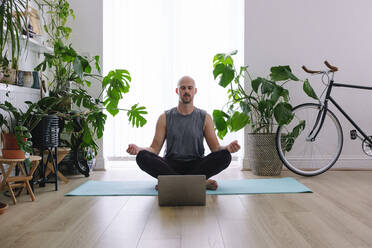 Man with eyes closed meditating in living room at home - ASGF02596