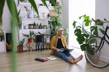 Man using laptop sitting on floor at home - ASGF02603