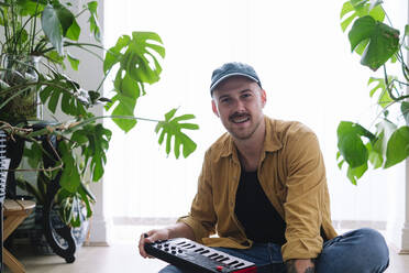 Smiling man with piano sitting on floor at home - ASGF02609