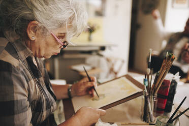 Ältere Frau malt mit Pinsel zu Hause - MRRF02333