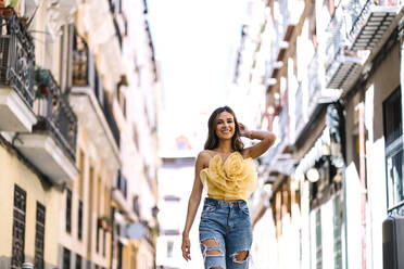 Smiling young woman walking amidst buildings - DAMF01076