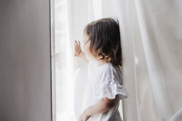 Little girl looking out of window at home - EBBF05848