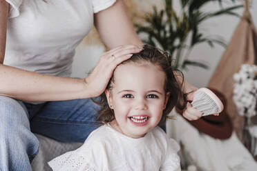 Mother brushing cute daughter's hair at home - EBBF05856