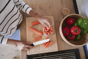 Woman putting slices of carrots in jar at home - EBBF05872