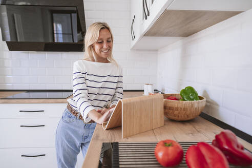 Lächelnde Frau mit Tablet-PC auf dem Küchentisch zu Hause - EBBF05884
