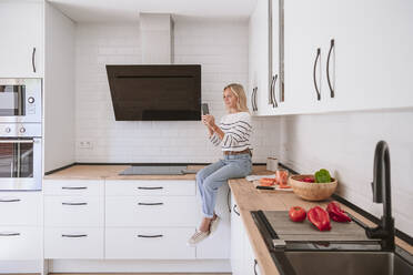 Woman using mobile phone in domestic kitchen at home - EBBF05891