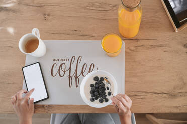 Woman using smart phone and having breakfast at home - EBBF05902