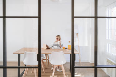 Woman with coffee cup using tablet PC on table at home - EBBF05906