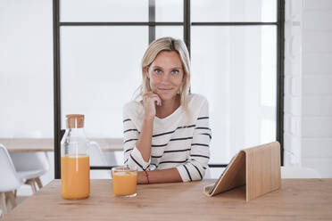 Junge Frau mit Saftglas und Tablet-PC auf dem Tisch zu Hause - EBBF05916