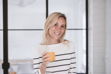 Lächelnde Frau mit Orangensaftglas in der Hand zu Hause - EBBF05918