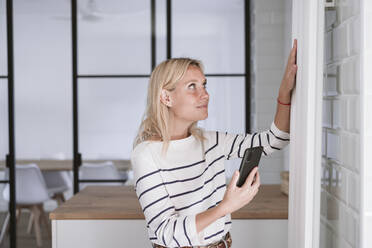 Woman with smart phone touching radiator at home - EBBF05931