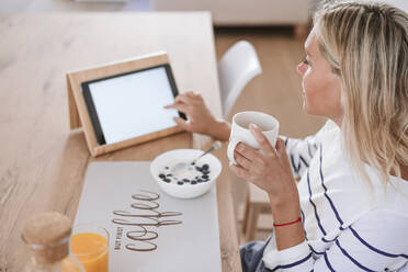 Junge Frau benutzt einen Tablet-PC und trinkt zu Hause einen Kaffee - EBBF05940