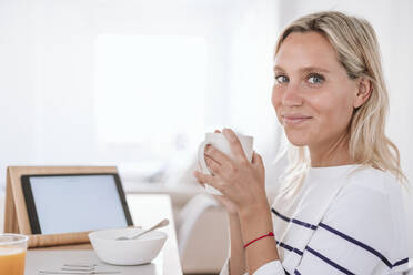 Lächelnde junge Frau beim Kaffee trinken zu Hause - EBBF05941