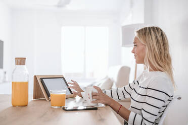 Young woman with coffee cup using tablet PC on table at home - EBBF05942