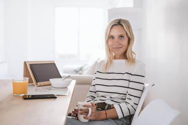 Smiling woman with coffee cup and tablet PC on table at home - EBBF05943