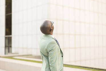 Businessman looking up standing in front of building at financial district - JCCMF07071