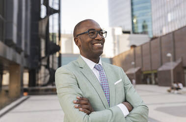 Happy businessman with arms crossed standing at financial district - JCCMF07091