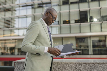 Businessman examining documents standing at financial district - JCCMF07101