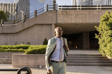 Mature businessman with backpack walking in financial district - JCCMF07115