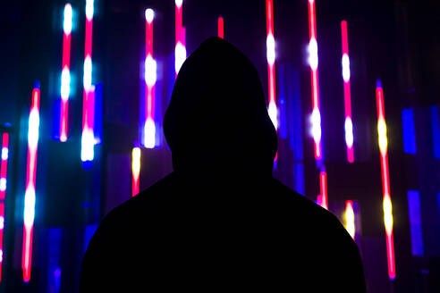 Man wearing hooded shirt in front of illuminated lights - MEUF07831