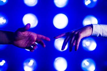 Hands of couple reaching towards each other in front of illuminated lights - MEUF07832