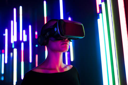 Frau trägt Virtual-Reality-Simulator in der Nähe von bunten Lichtern - MEUF07855