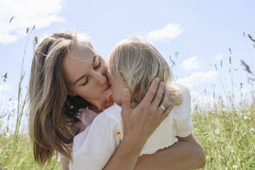 Mother kissing daughter on sunny day at field - EYAF02032