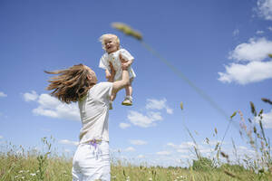 Cheerful woman with daughter enjoying on field - EYAF02033