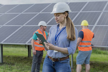 Frau mit Tablet-PC und Kollegen im Hintergrund in einer Solarstation - OSF00649