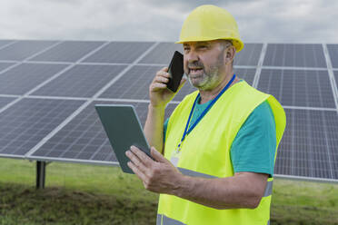 Ingenieur, der einen Tablet-PC hält und über ein Smartphone mit Sonnenkollektoren spricht - OSF00651