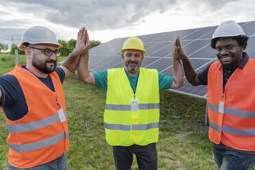 Smiling engineers giving high five to each other at solar power station - OSF00661