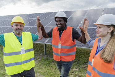 Smiling multiracial engineers giving high five to each other at solar power station - OSF00662
