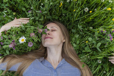 Smiling mature woman smelling flowers lying on grass at field - OSF00670
