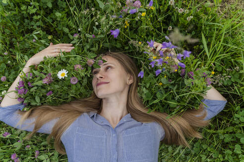 Lächelnde Frau inmitten von Blumen auf einem Feld liegend - OSF00671