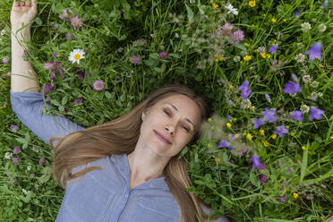 Happy mature woman lying on grass at field - OSF00672