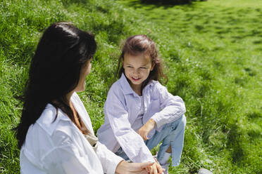 Lächelndes Mädchen im Gespräch mit ihrer Mutter auf einer Wiese an einem sonnigen Tag - SEAF01159