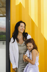 Glückliche Mutter und Tochter stehen vor einer gelben Wand - SEAF01165