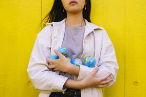 Young woman with globes standing in front of yellow wall - ASGF02622