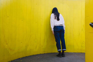 Depressive junge Frau lehnt an gelber Wand - ASGF02627