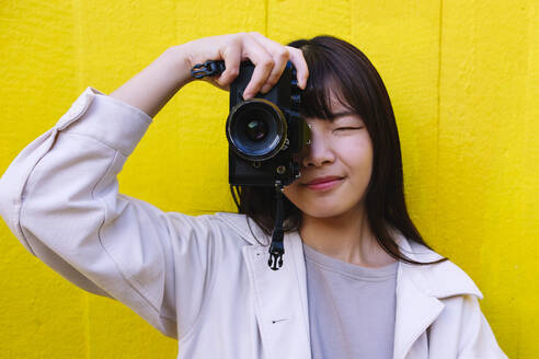 Junge Frau beim Fotografieren mit Kamera vor einer Wand - ASGF02660